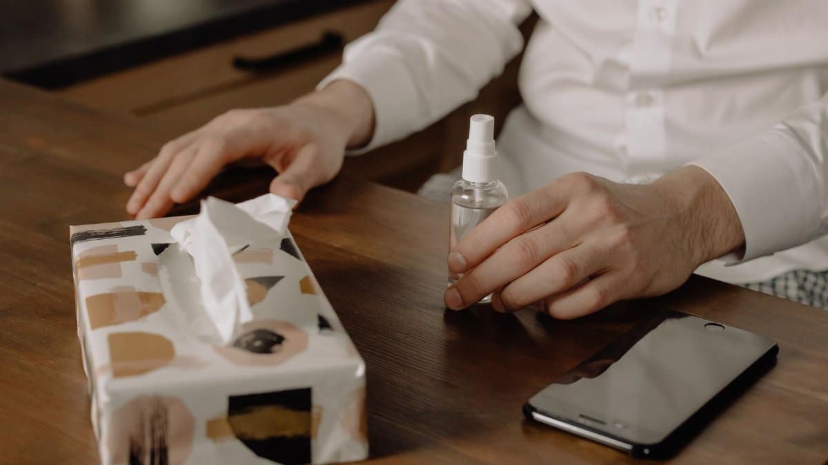 A person using hand sanitizer with tissues and phone on a wooden table, promoting hygiene.