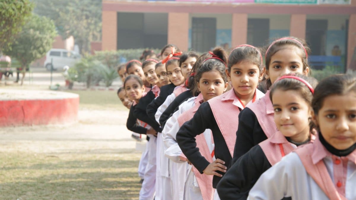 A group of school girls in uniform lined up outdoors, hands on waists, showing unity and discipline.