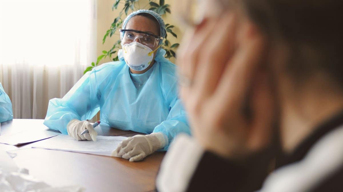 Healthcare professional in protective gear consulting with a patient indoors.