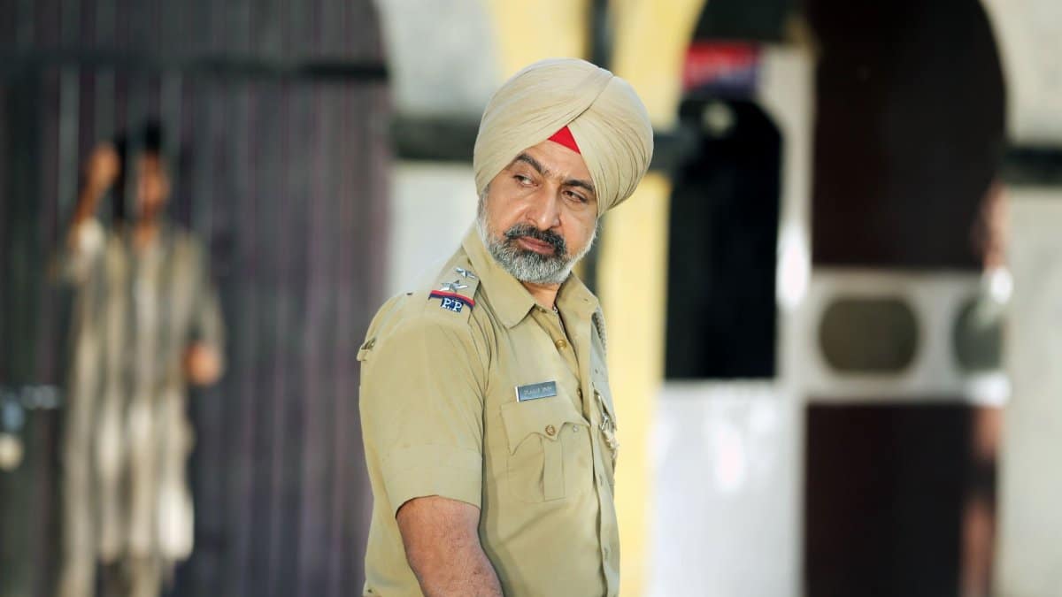 Sikh police officer in uniform standing outdoors with focused expression.