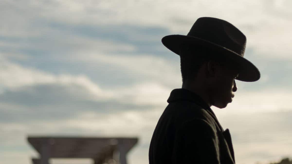 Silhouetted profile of a man in a fedora against a cloudy sky, evoking mystery and contemplation.
