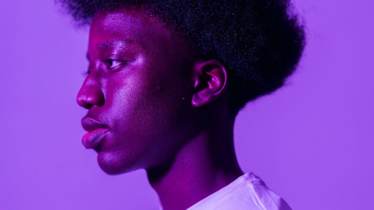 Profile portrait of a young man with afro hair against a vibrant purple background.