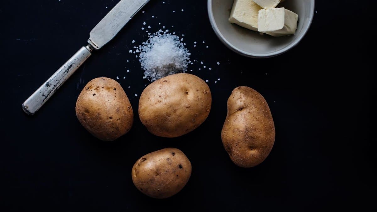 High contrast image of potatoes, butter, and salt on a dark background.