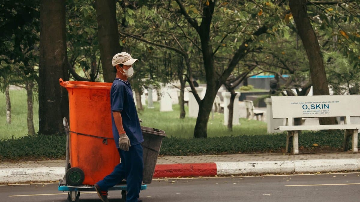 A street worker collects trash in a park, emphasizing urban cleanliness.