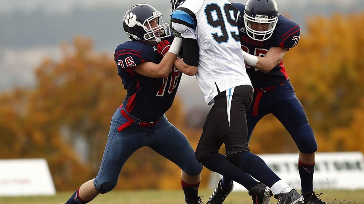 Football players in action during a competitive game on a field with autumn foliage.