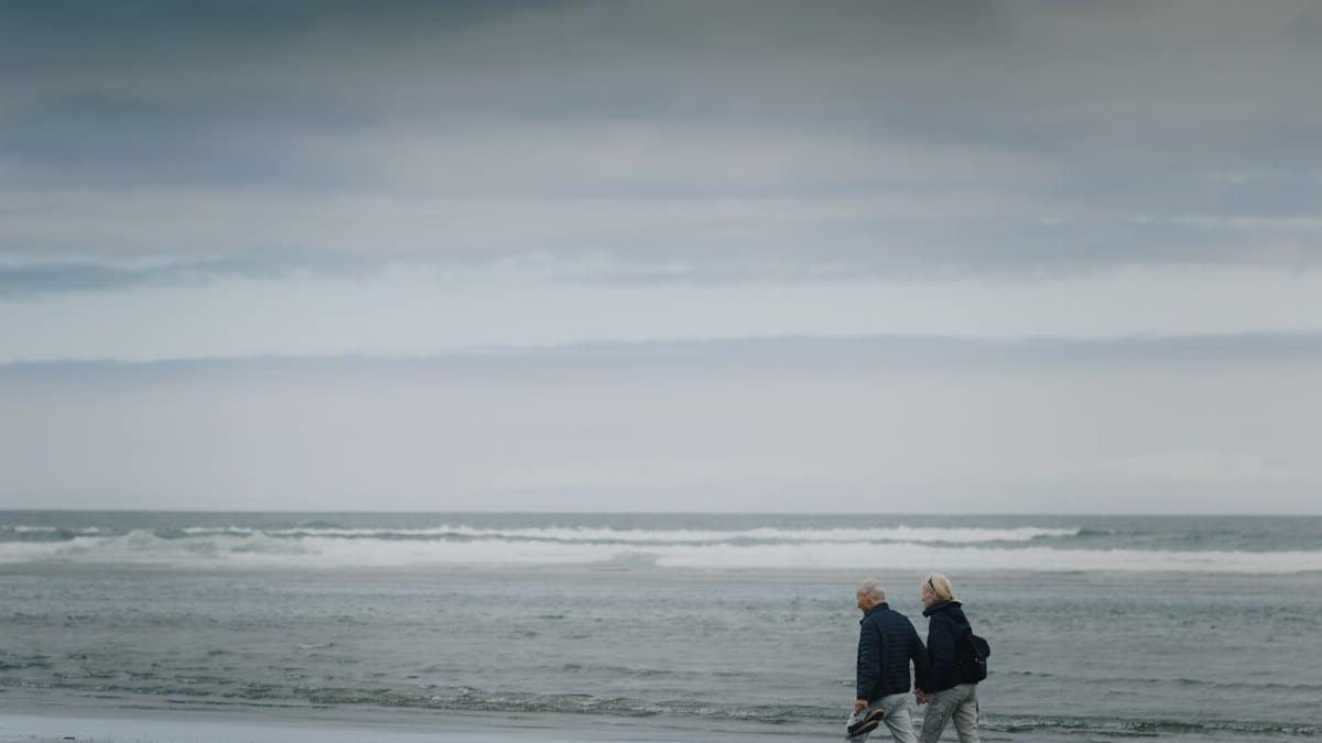 Two senior adults walking on a gloomy beach, offering a sense of serenity and reflection.