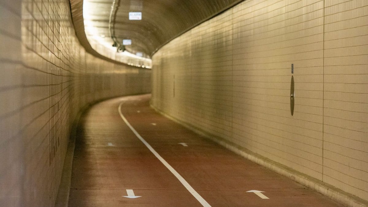A well-lit curved tunnel with a bicycle lane and directional arrows on the floor.
