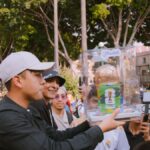 Group of people celebrating with a FIFA World Cup trophy replica in a vibrant outdoor setting.