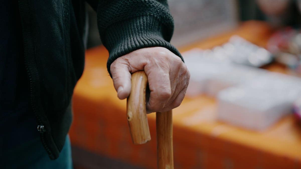 Close-up of a senior adult's hand gripping a wooden cane indoors.