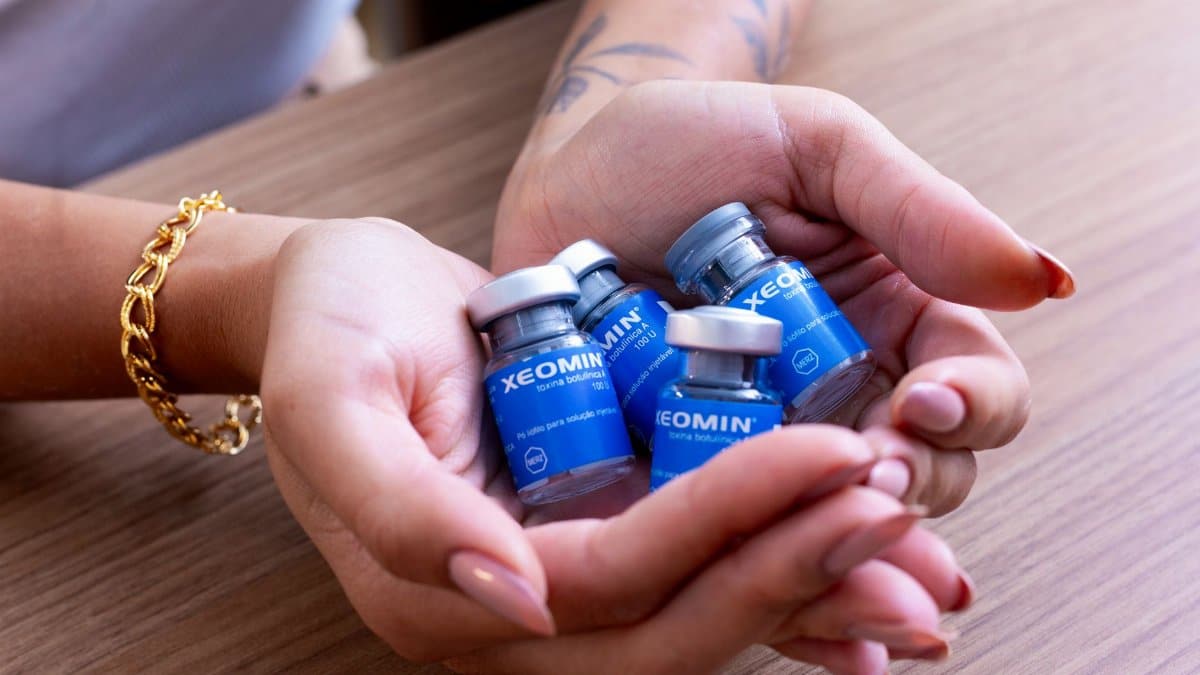 Female hands cradle Xeomin botulinum toxin bottles on a wooden table.