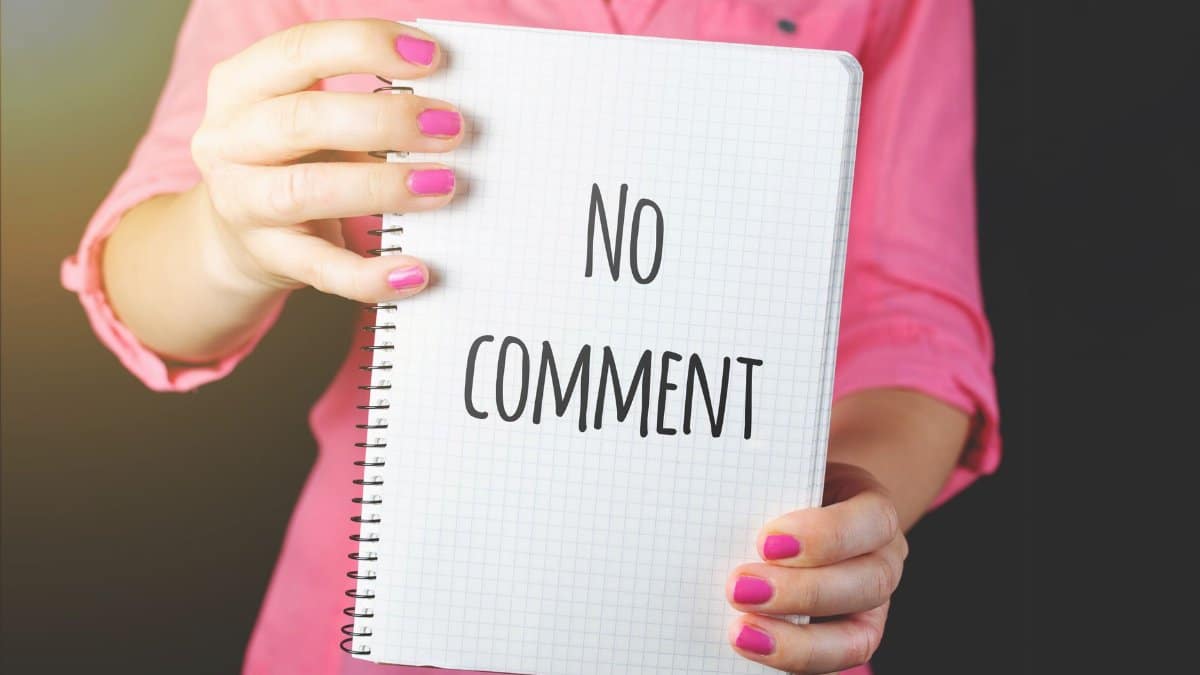 A woman in a pink shirt holds a notebook with 'No comment' text visible, conveying silence or privacy.