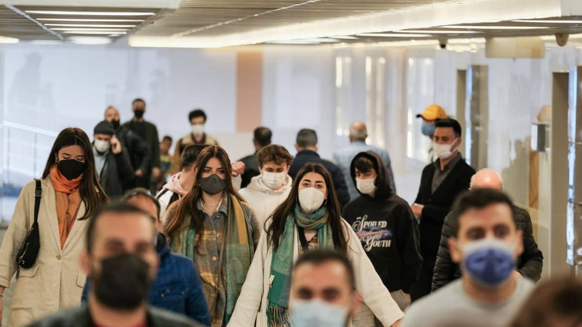 A diverse group of people wearing face masks walking indoors during the pandemic.