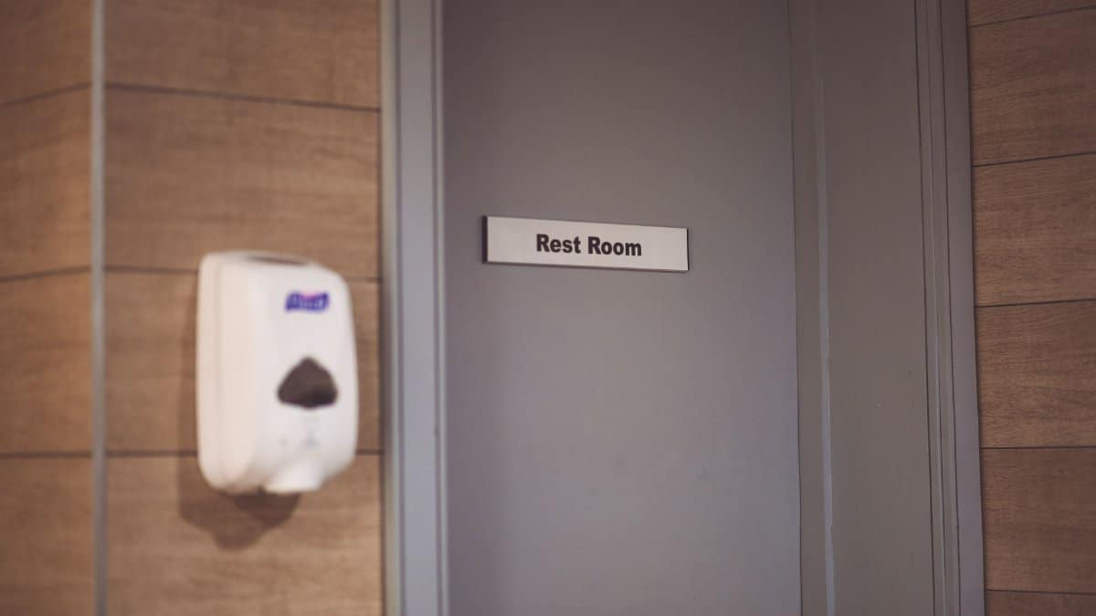 Image of a soap dispenser and a restroom door sign in a public restroom.