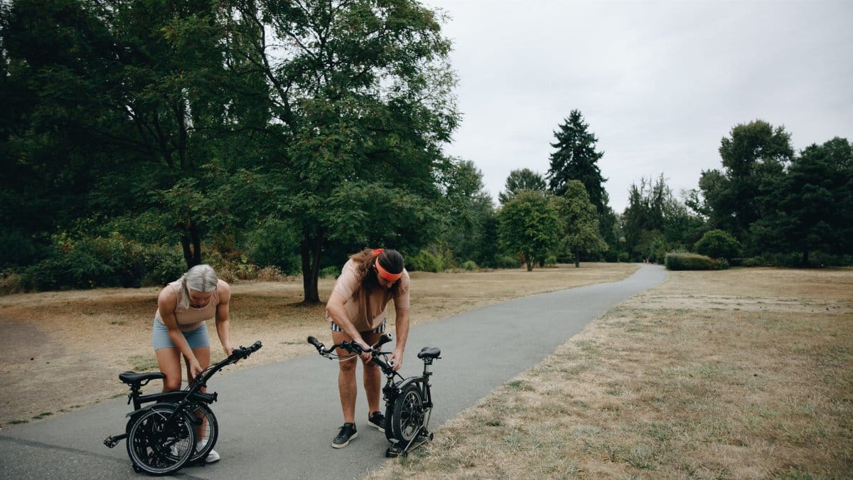 A couple adjusting their bicycles on a park pathway during a cloudy day, enjoying an outdoor activity.