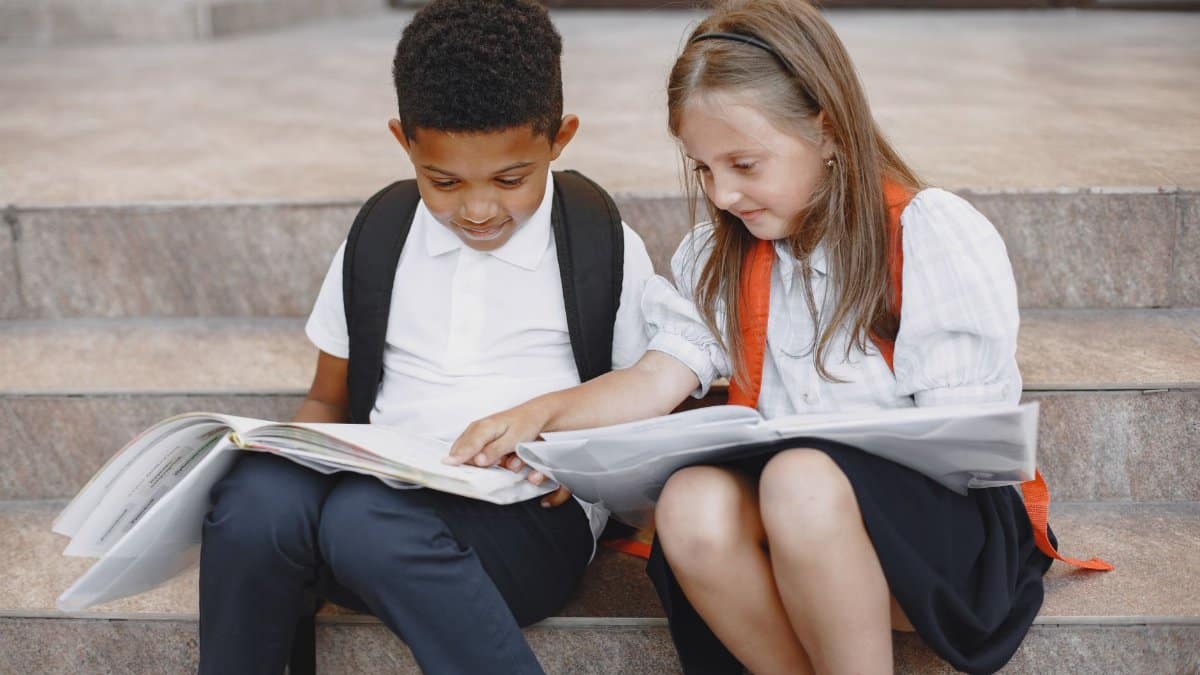 Two students sit on steps reading books outside a school building.