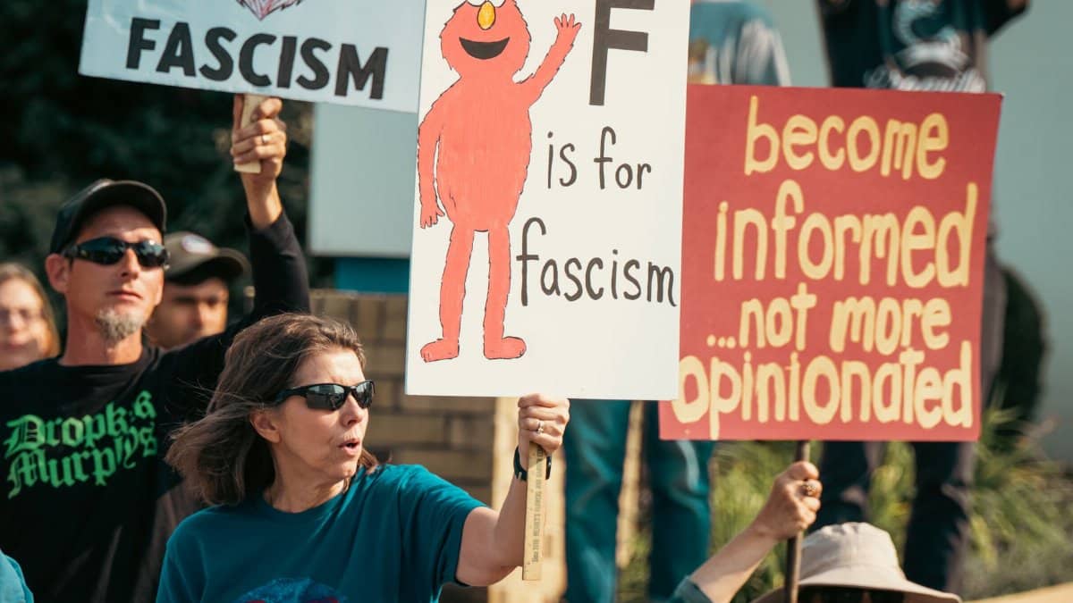 Protesters at a rally holding anti-fascism and awareness signs, advocating for informed opinions.
