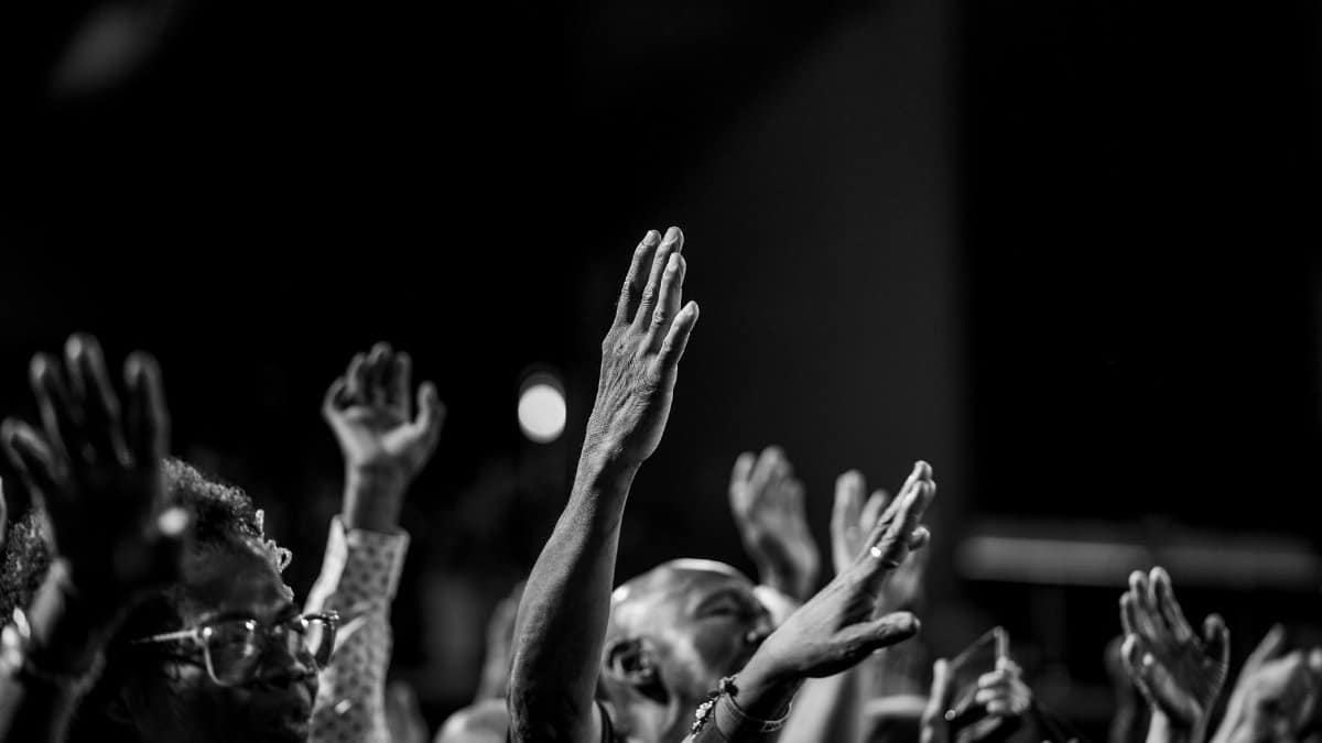 Monochrome photo capturing a group with hands raised in prayer and worship.