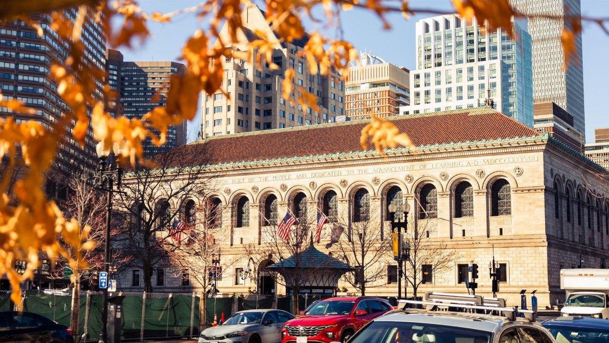 Historic Boston Public Library framed by autumn leaves in vibrant downtown cityscape.