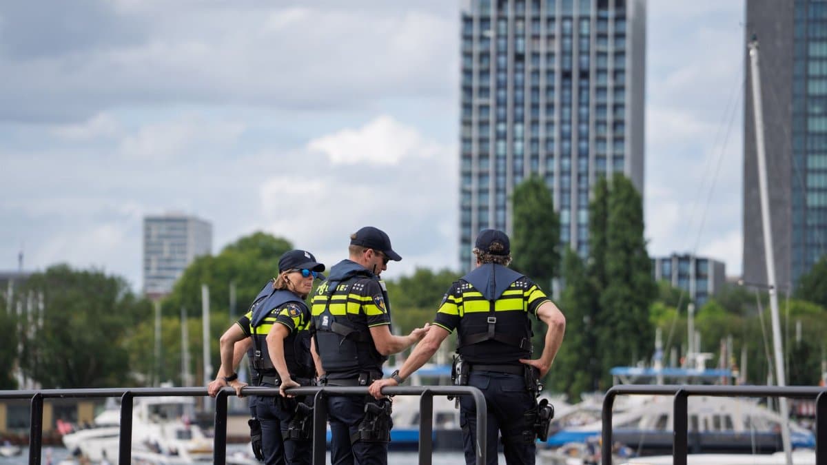 Three police officers stand on a waterfront railing, overseeing a cityscape with high-rise buildings.