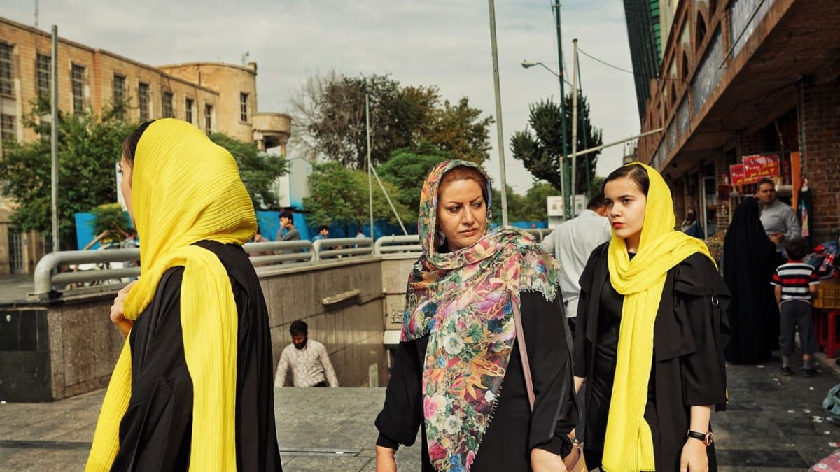 Women wearing headscarves and vibrant scarves walk on a sunny street in Iran, showcasing cultural fashion.