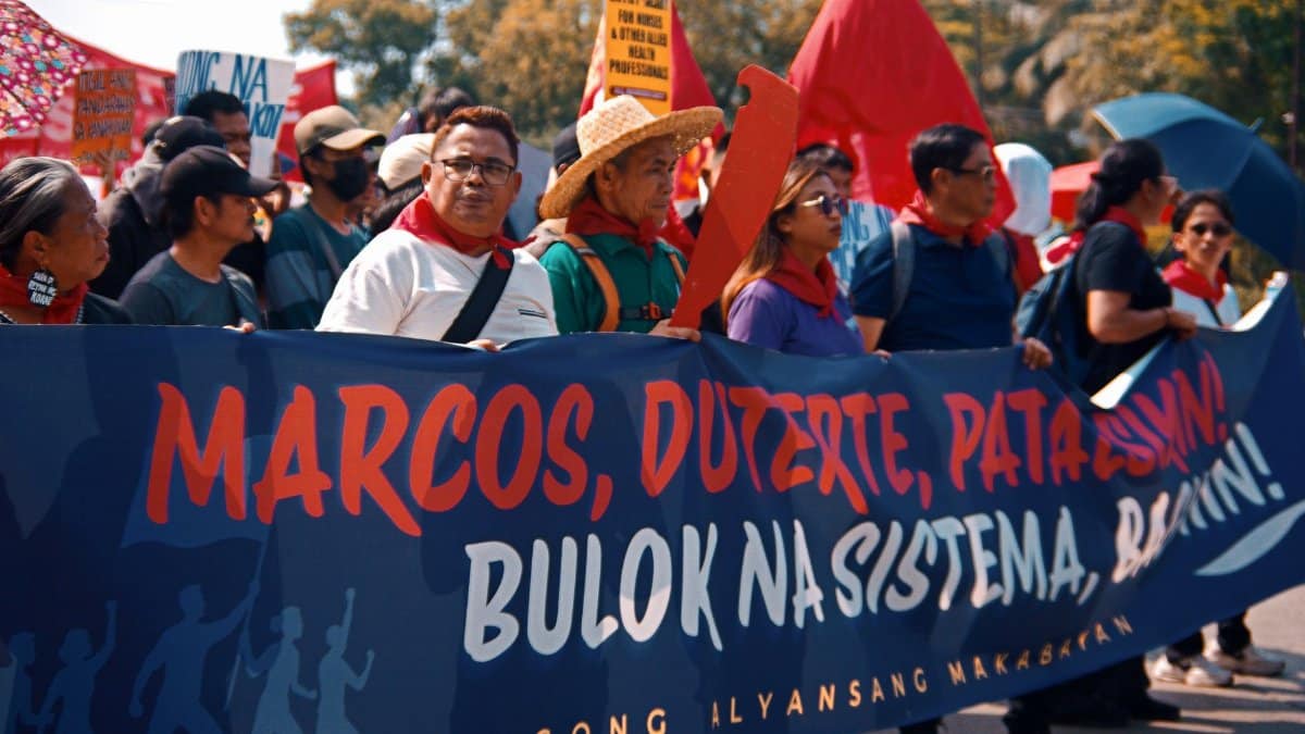 A group of protesters holding a banner during a daytime demonstration outdoors.