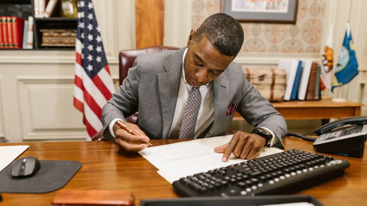 Professional man signs contract at desk in classic office environment.