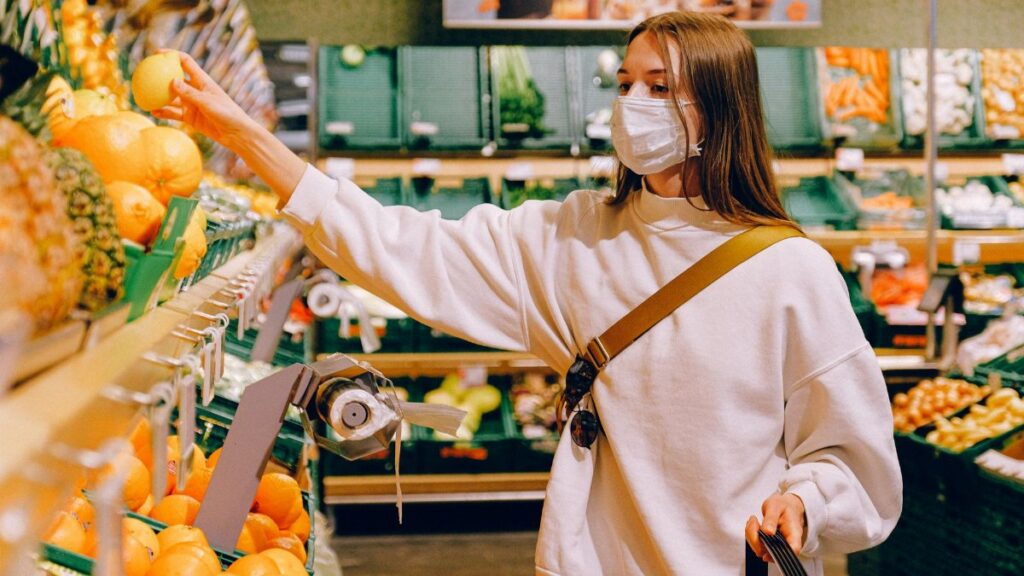 Woman wearing a mask selecting fruit at a grocery store during pandemic.