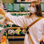 Woman wearing a mask selecting fruit at a grocery store during pandemic.