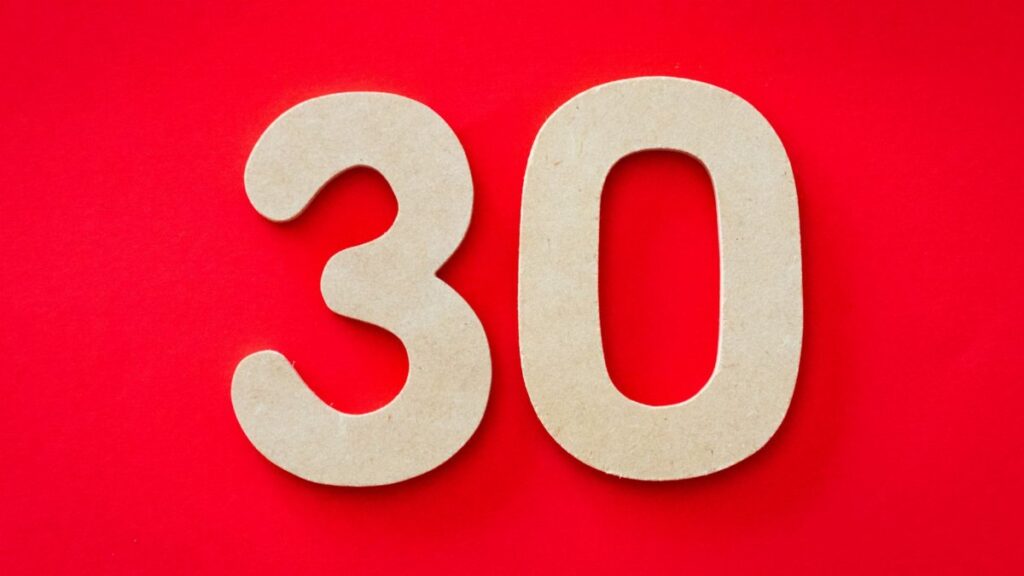 Close-up of cardboard number 30 on a bright red background, ideal for birthday or anniversary themes.