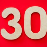 Close-up of cardboard number 30 on a bright red background, ideal for birthday or anniversary themes.