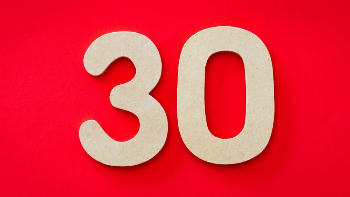 Close-up of cardboard number 30 on a bright red background, ideal for birthday or anniversary themes.