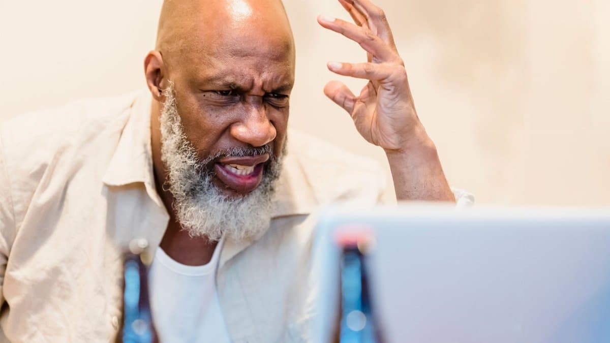 An adult man expressing frustration during a video call with a laptop indoors.