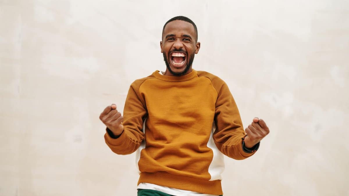 A joyful man with a beard in a sweater, expressing excitement and celebration indoors.