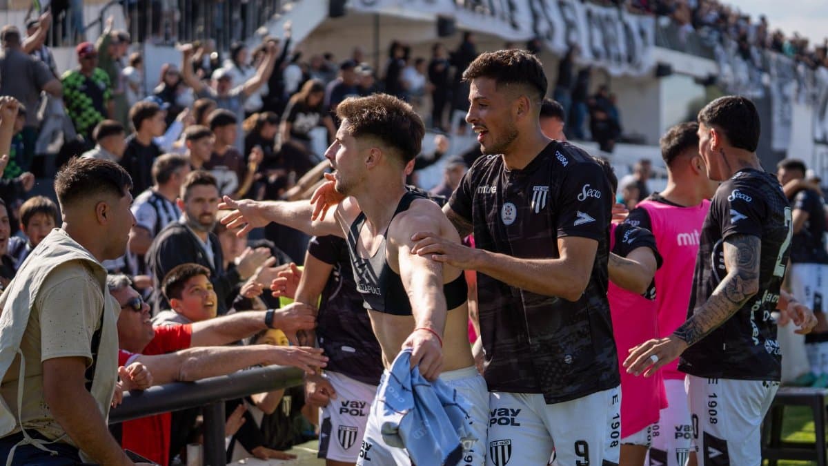 Excited soccer players celebrating a victory with cheering fans in a crowded stadium.