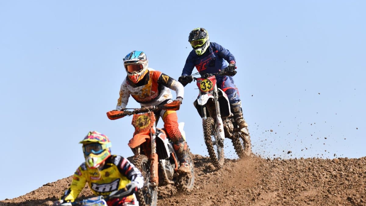 Three motocross riders competing on a dirt track, showcasing speed and skills.
