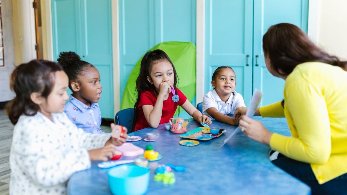 A group of preschoolers interacting with a teacher in a colorful classroom setting.