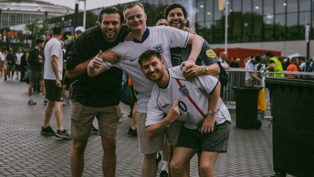 Group of enthusiastic football fans posing outside a stadium in England, showing camaraderie.