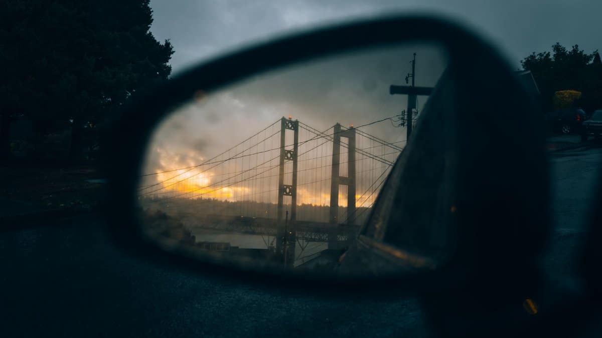 Reflection of the Tacoma Narrows Bridge captured in a car mirror during a colorful sunset in Tacoma, Washington.