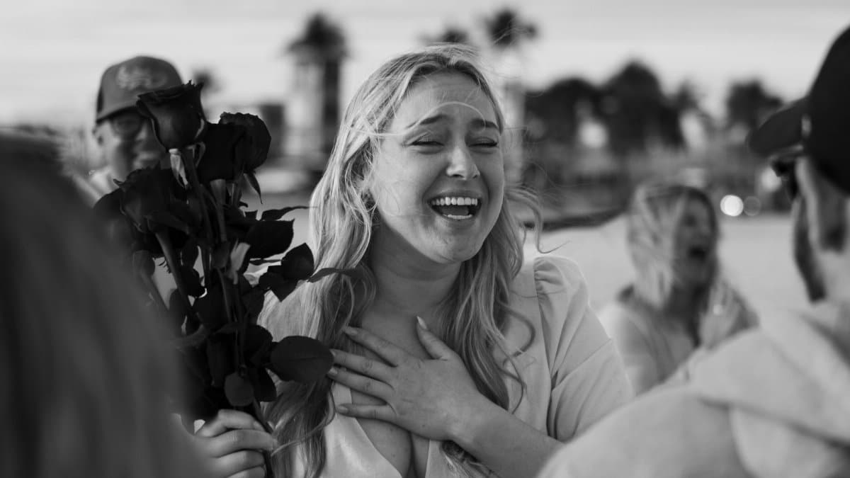 A joyful woman holding roses outdoors, captured in black and white, expressing strong emotions.