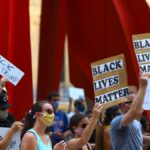 Protesters gather with signs supporting Black Lives Matter and denouncing Donald Trump in a peaceful rally.