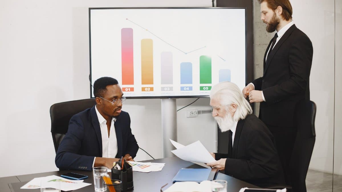 Three businessmen discussing financial data in a modern office setting with charts.