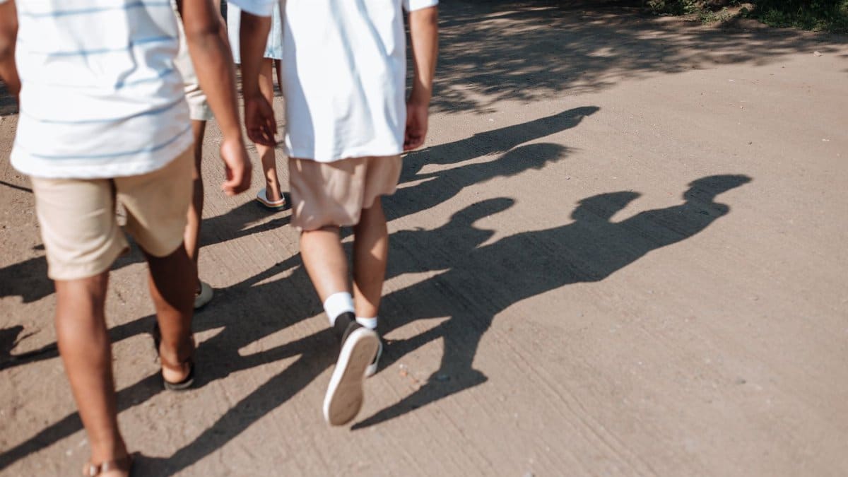 A group of teenagers walking on a sunlit dirt path during summer, casting long shadows.