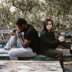 A couple sits back to back on a wooden bench, indicating a disagreement or breakup.