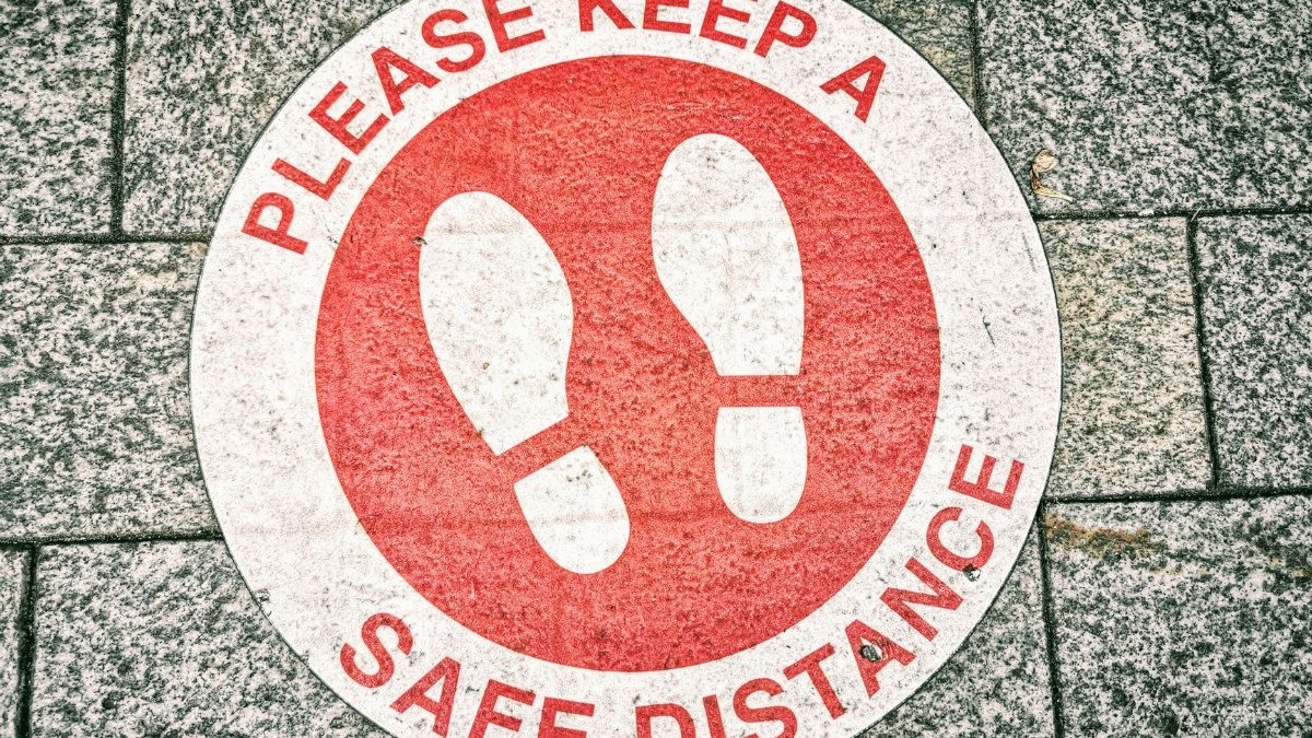 Close-up of a social distancing sign on pavement urging safe distance.