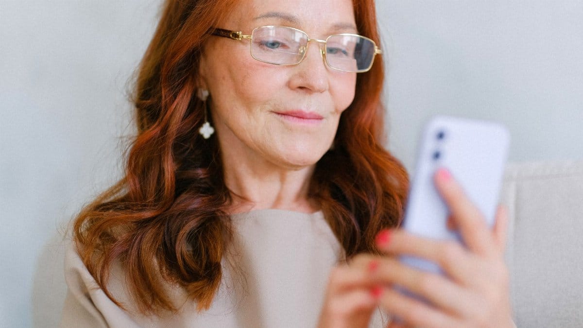 Elegant middle-aged woman with glasses using a smartphone indoors.