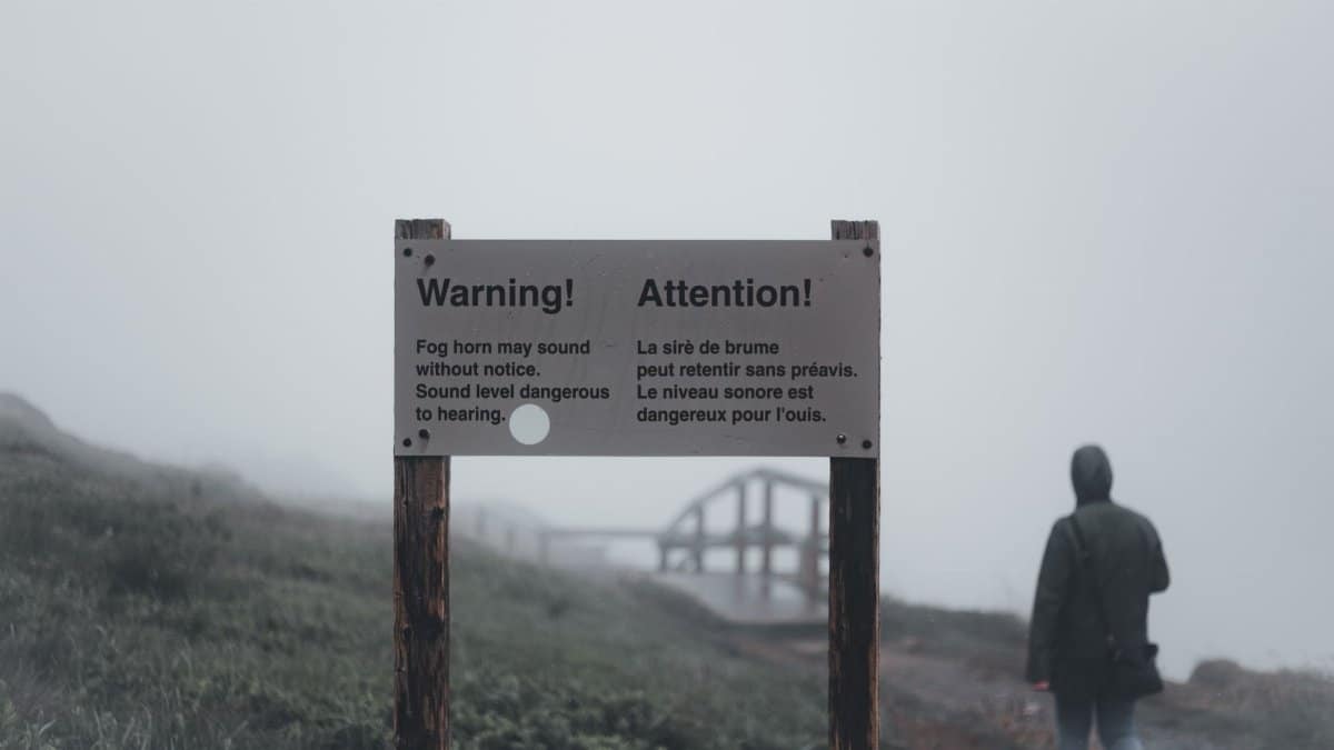 A foggy landscape with a warning sign and a lone person walking away, creating a mysterious atmosphere.