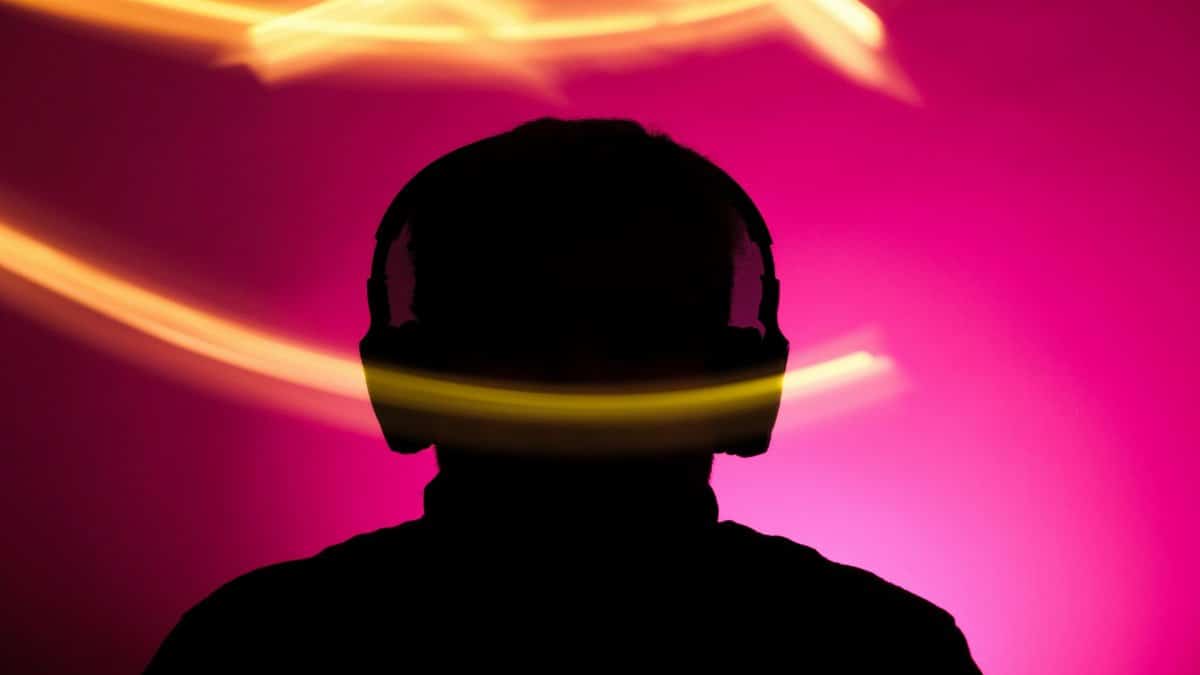Silhouette of person with headphones against vibrant pink background and dynamic light streaks.