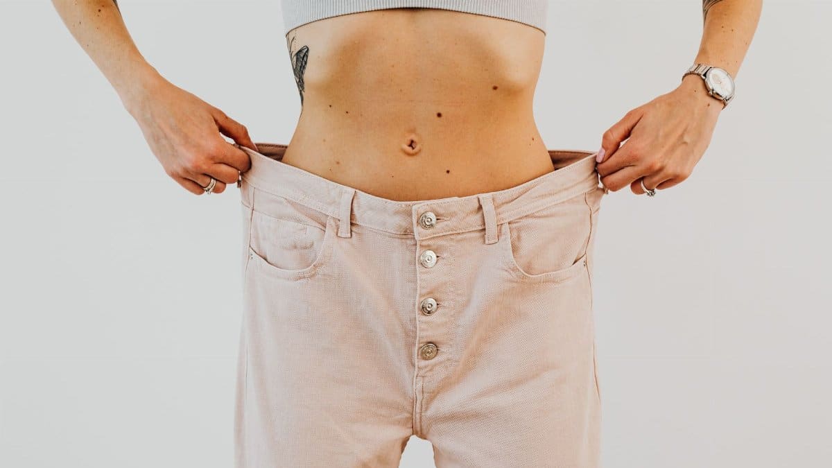 Close-up of a woman holding oversized pants at her waist, showcasing significant weight loss.
