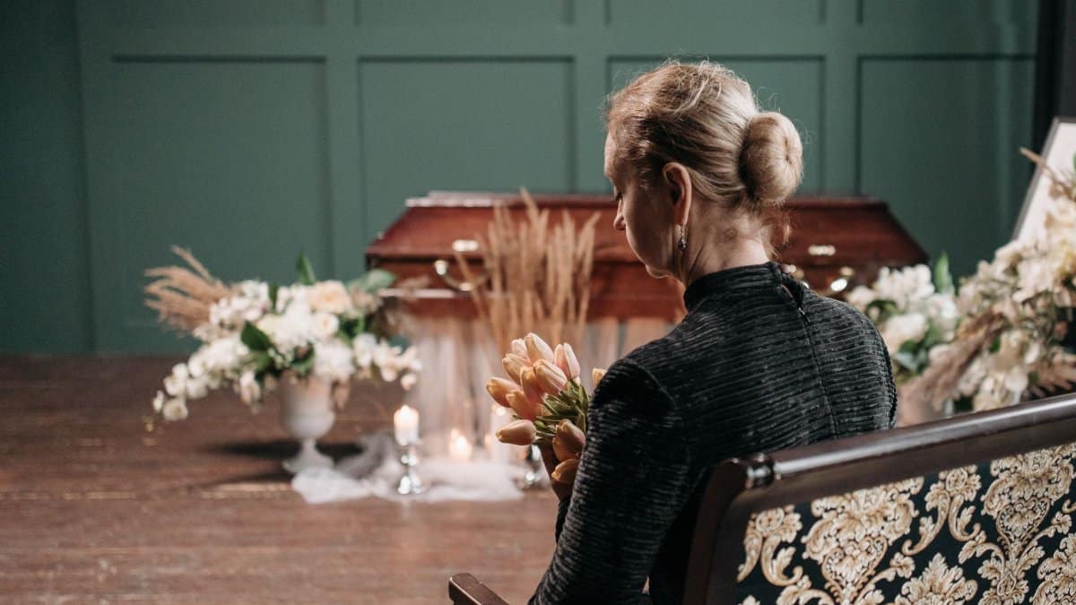 A woman in mourning holding flowers at a funeral, highlighting grief and remembrance.