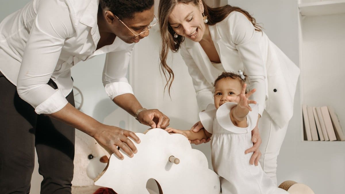 A joyful family moment with parents playing with their toddler on a rocking horse indoors.